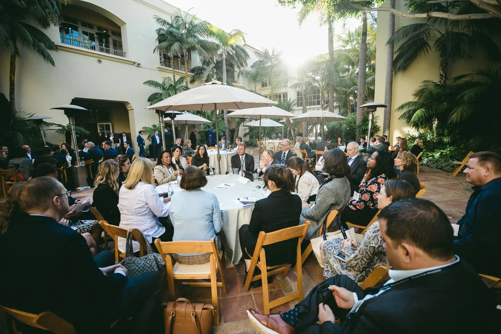 MFA members, staff, and leaders of hedge funds talking at round tables in the courtyard of an outdoor networking event.